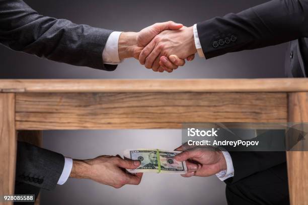Businesspeople Shaking Hands And Taking Bribe Under Table Stock Photo - Download Image Now