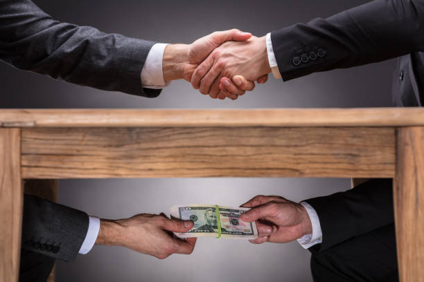 businesspeople shaking hands and taking bribe under table - bribing imagens e fotografias de stock