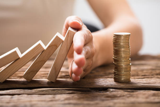Close-up Of A Businesswoman's Hand Stopping Falling Blocks Close-up Of A Businesswoman's Hand Stopping The Wooden Blocks From Falling On Stacked Coins hand stopping dominos stock pictures, royalty-free photos & images