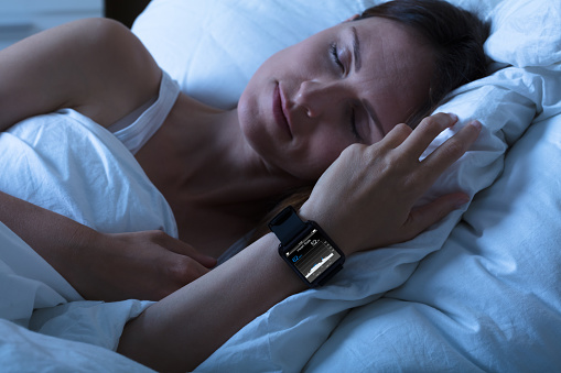 Close-up Of A Woman Sleeping With Smart Watch Showing Heartbeat Rate On Bed