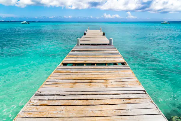 A old dock in Grand Cayman Island in the Caribbean with blue sky and boats on the horizon.