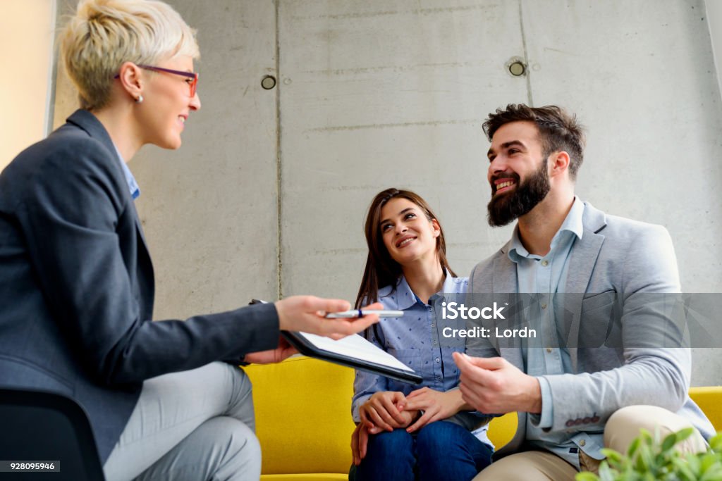 Young married couple at their counselor young married couple with real estate agent, financial advisor or marriage counselor Real Estate Agent Stock Photo