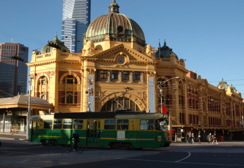 The entrance to Flinders Street Train Station in Melbourne, Australia with a traditional green tram passing in front.