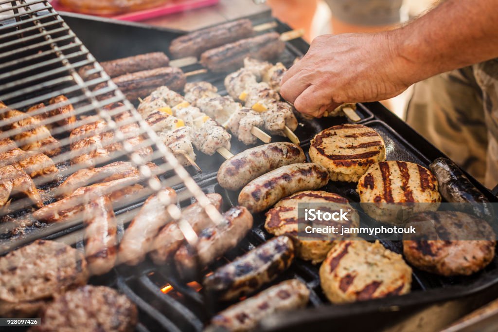 Gas barbecue cooking a variety of meat Cooking on a gas barbecue outside in the sunshine. With chicken, sausages, kebabs, burgers and fish cooking on the griddle. Barbecue Grill Stock Photo
