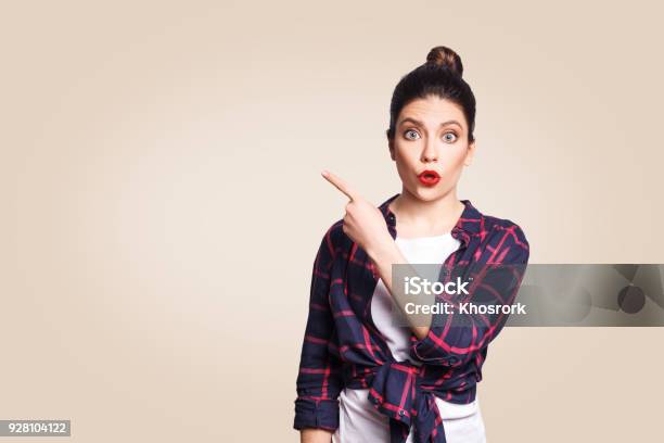 Foto de Young Surpreendeu A Menina Com Cabelo Casual Estilo E Bun Apontando O Dedo Para Os Lados e mais fotos de stock de Estupefação