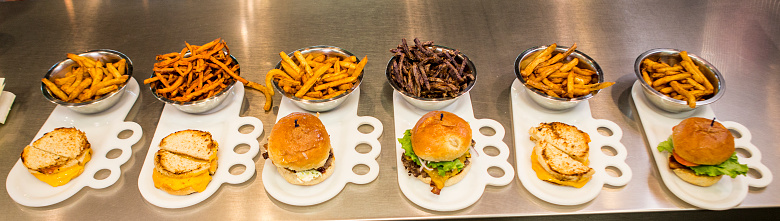 Various hamburger and french fries lined up on a restaurant kitchen counter.
