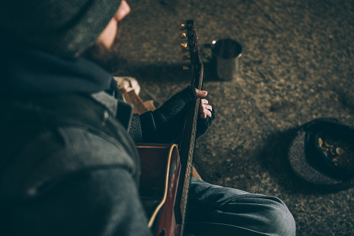 One man, young homeless man playing acoustic guitar on the street and begging.