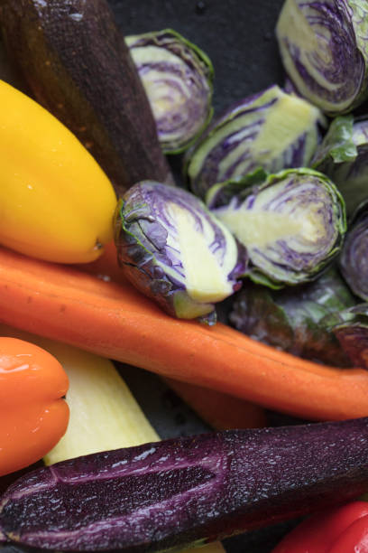 Mixed purple Brussels Spouts, colorful carrots and yellow, red and orange bell peppers being prepped for pan roasting in the oven