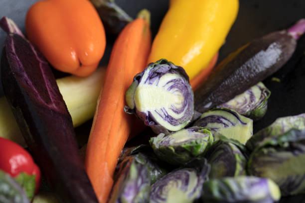 Mixed purple Brussels Spouts, colorful carrots and yellow, red and orange bell peppers being prepped for pan roasting in the oven