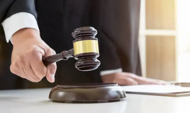 Photo of Close up of Male lawyer or judge hand's striking the gavel on sounding block, working with Law books, report the case on table in modern office, Law and justice concept