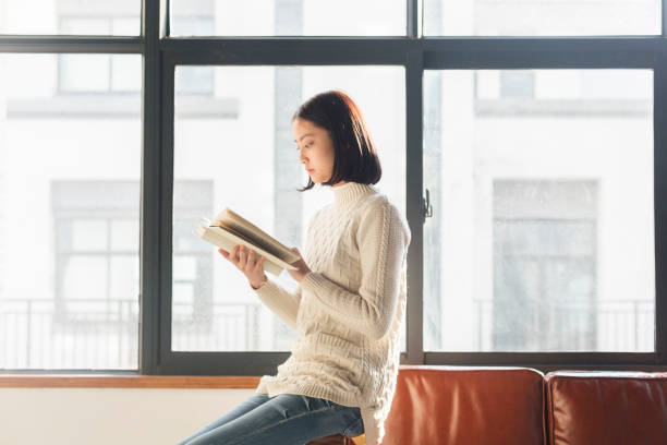 istock young woman reading a book by window 928162014