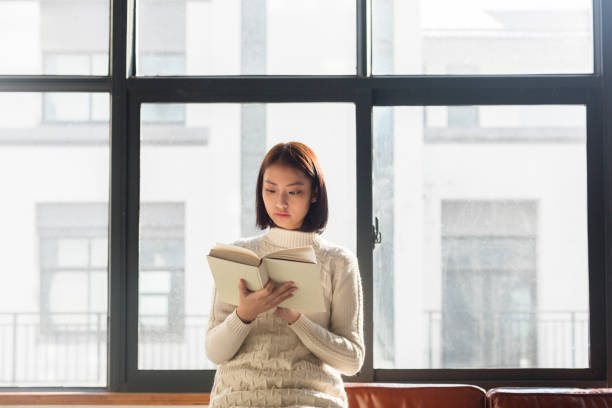 istock young woman reading a book by window 928162034