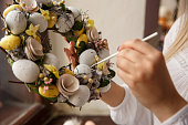 Girl paints on handmade wreath with Easter eggs. Woman draws on Easter eggs. Preparation and celebration of Easter holiday