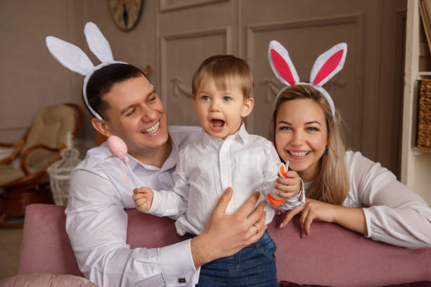 heureux parents et enfant célébrant le jour de pâques. mère et père portant des oreilles de lapin et d’embrasser leur fils. concept de pâques joyeux - easter rabbit bizarre women photos et images de collection
