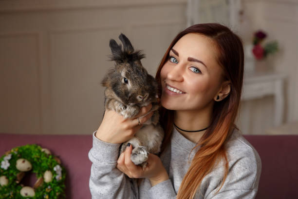istock Happy woman holding Easter bunny and smiling to camera on spring wreath with Easter eggs background 928167342