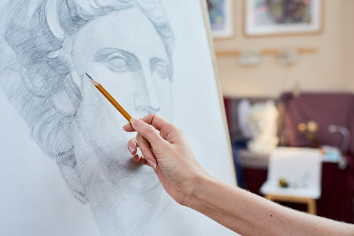 Close-up of unrecognizable woman drawing sculpture bust and applying lines to make shadow on paper