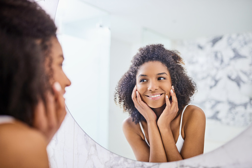 Shot of an attractive young woman admiring her face in the bathroom mirror