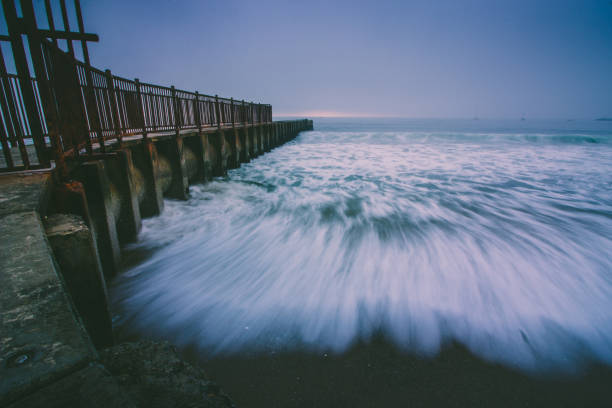 A small wave breaks near the timbers of a vintage pier at sunset. California 2013