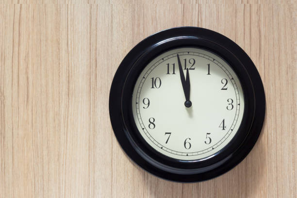 black steel clock wall on wooden background at mid day time