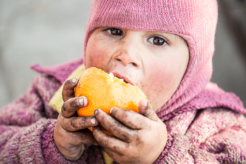 Indian baby eating oranges with dirty hand, looking directly at camera