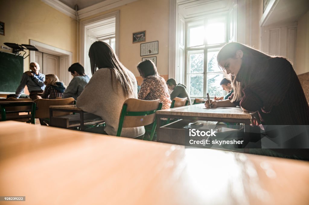 Group of high school students having a test in the classroom. Large group of teenage students sitting in the classroom while having a mid-term test. Educational Exam Stock Photo