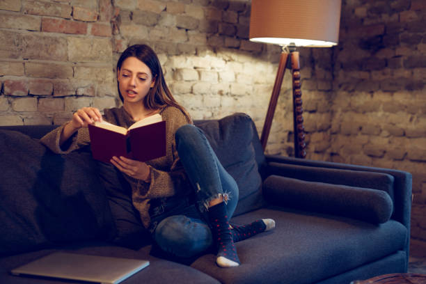 istock Young woman sitting on sofa reading a book 928239660