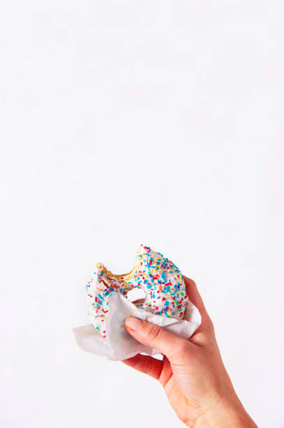 istock Woman's hand is holding a half eaten bagel in front of white background. 928242558