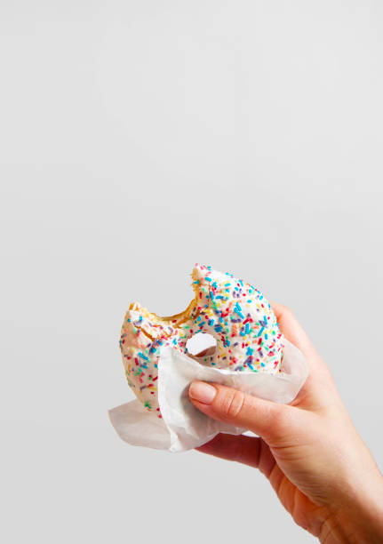 istock Woman's hand is holding a half eaten bagel in front of white background. 928242588