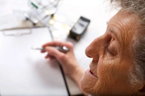 Senior woman between 70 and 80 years old is making some calculation. Top view