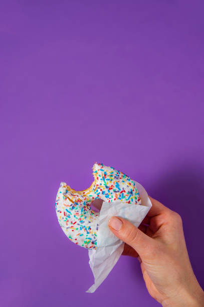 Woman's hand is holding a half eaten bagel in front of purple background. stock photo