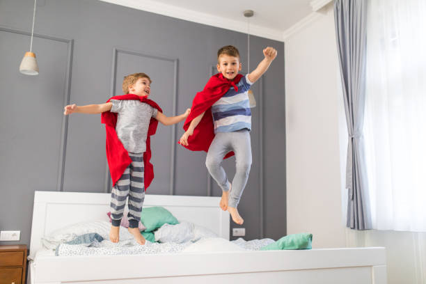 istock Two playful boys having fun while jumping on a bed and pretending to be superheroes. 928254686