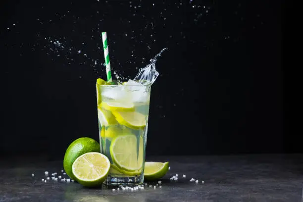 fresh summer caipirinha cocktail with splash on a black background. green fruit lime on table