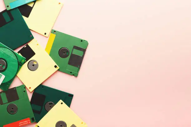 Old floppy disks isolated on pink background. Border of magnetic retro storage devices, cutout of colorful diskettes, copy space, flat lay, top view