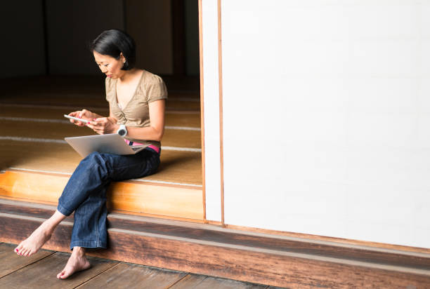 side, front view of woman sitting on temple podium, looking at tabled while having laptop on her knees, smiling and enjoying zen garden of chion-ji temple in kyoto, japan - zen like women temple meditating zdjęcia i obrazy z banku zdjęć