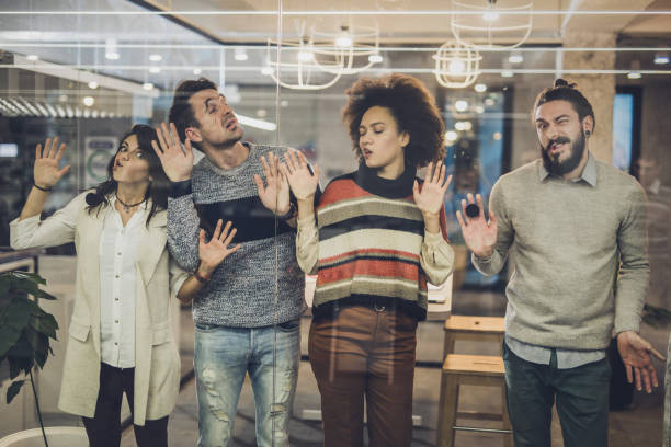Playful colleagues having fun while sticking their faces on glass wall.