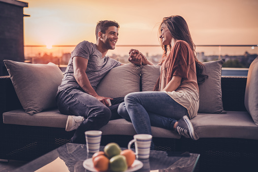 Happy couple holding hands while talking on a penthouse terrace at sunrise.