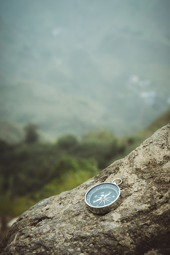Trakking concept - Analogical Compass laying on the rocks with mountains in background.