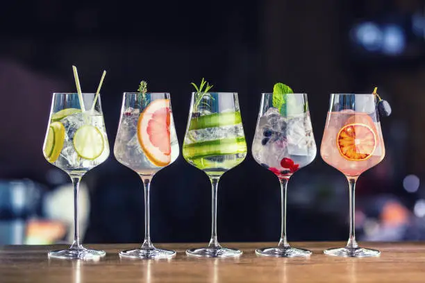 Photo of Five colorful gin tonic cocktails in wine glasses on bar counter in pup or restaurant