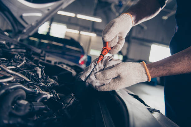 primo piano ritagliato colpo di esperti specialista meccanico professionale controllo del livello dell'olio nel motore auto con strumento arancione, in officina. manutenzione, sicurezza, cofano aperto supportato di auto - car examining mechanic auto mechanic foto e immagini stock