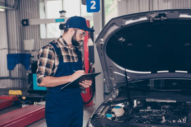istock Expert professional engineer at mechanical work shop, in special safety outfit uniform, checkered shirt, hat head wear, filling the form of automotive breakdown, focused, serious, concentrated 928323982