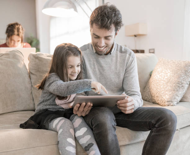 istock Father using tablet with daughter while mother is working with her laptop at home 928336288