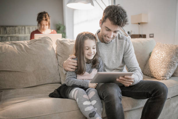 istock Father using tablet with daughter while mother is working with her laptop at home 928336300