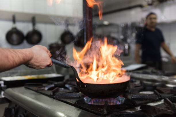 istock Chef cooking with flame in a frying pan on a kitchen stove. 928337348