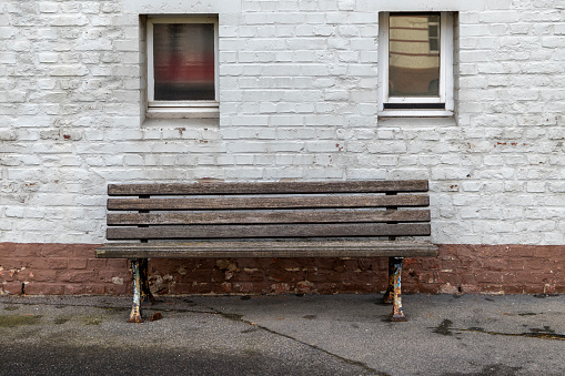 Single wooden bench in front of a white house facade with 2 windows