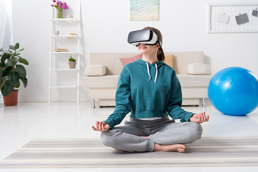 girl sitting in lotus position with virtual reality headset at home