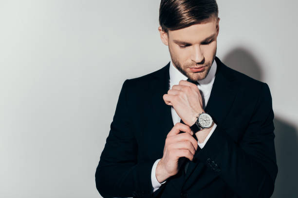 istock Thoughtful confident businessman in suit fixing his watch on white background 928348696