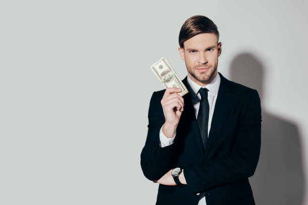 istock Young confident businessman in suit showing dollar banknote looking at camera on white background 928351710