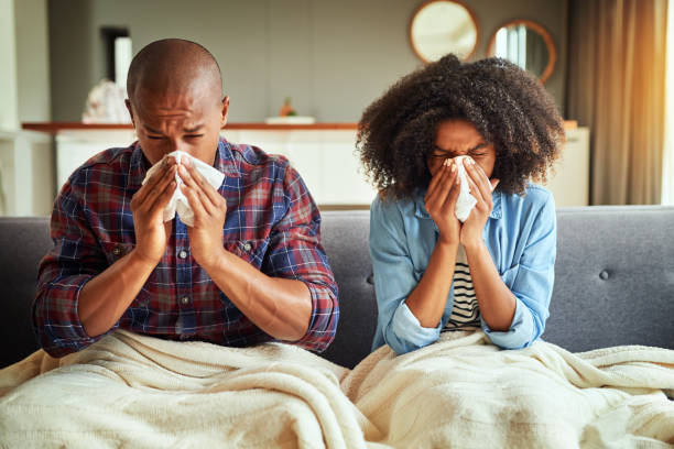 How did we both get sick? Shot of a tired looking young couple seated on a couch with blankets while being sick together at home cold virus stock pictures, royalty-free photos & images
