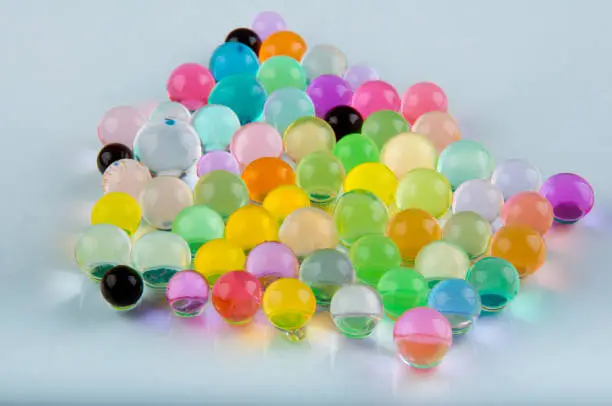 Multicolored gel balls lay on glass surface on white background