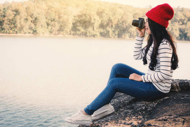 istock Woman Photographing While Sitting On Rock At Lakeshore 928374584